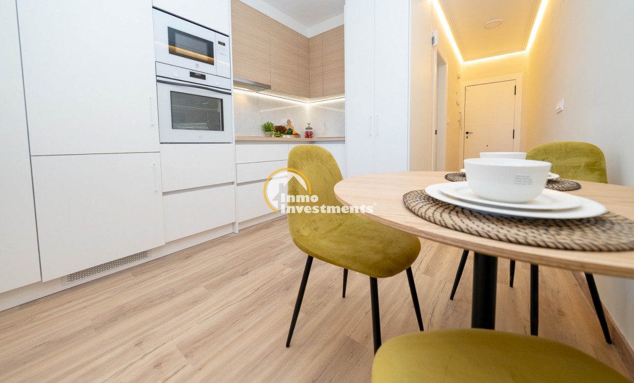 Open-plan kitchen-diner in Ciudad Quesada apartment with built-in oven, white cabinets, wood worktops and round dining table