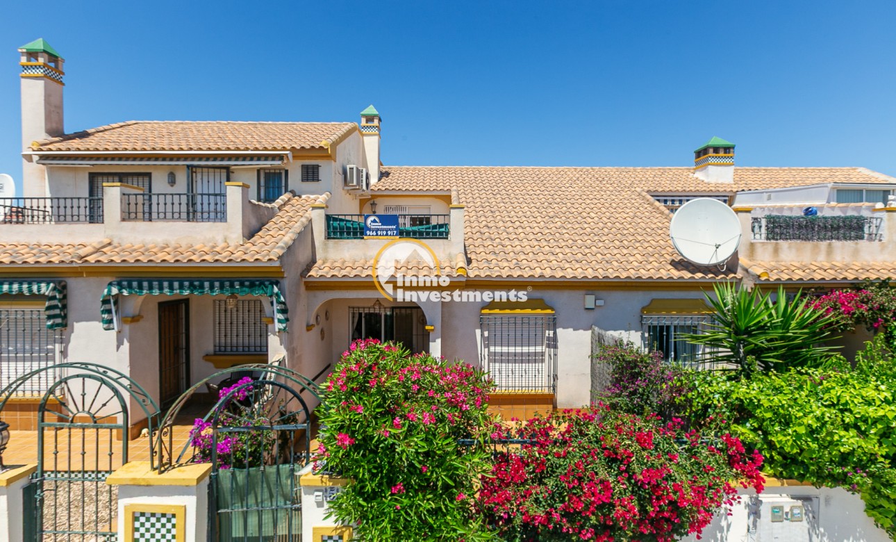 Front elevation of La Zenia town house with terracotta roof, gated terrace, awnings, satellite dish and flowering shrubs